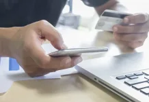 A man holding mobile phone and credit card on laptop for online
